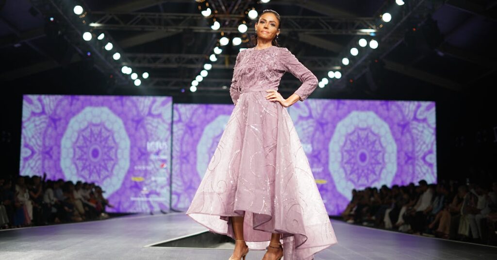 Model in elegant dress poses on a vibrant fashion show runway.
