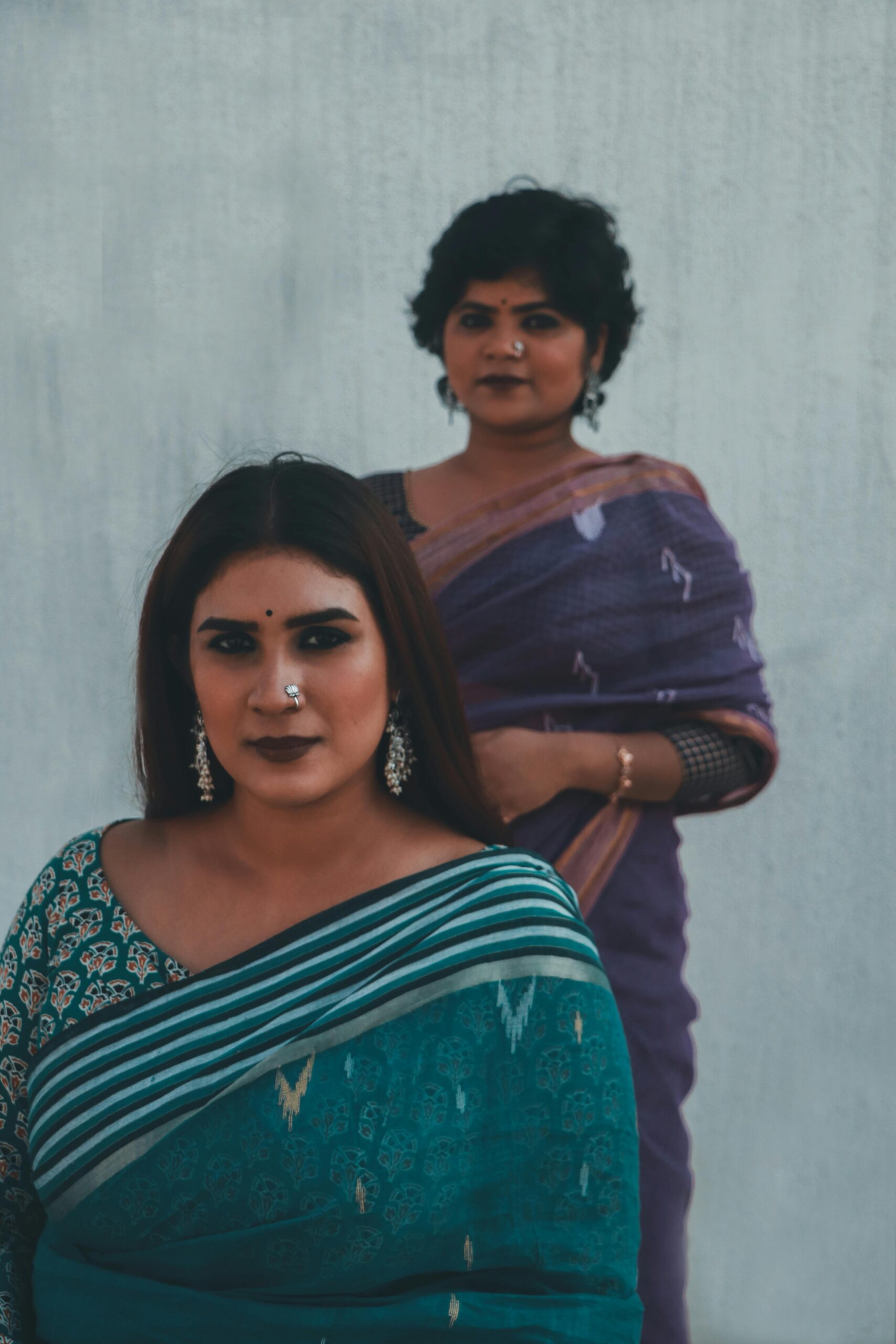 Two Indian women in sarees posing with elegance and grace, highlighting cultural beauty.
